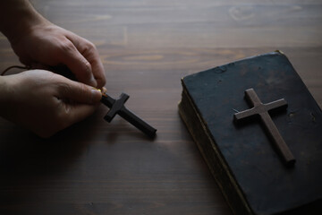 Hands Holding Wooden Cross with Old Bible on Wooden Surface - Religious Faith Concept