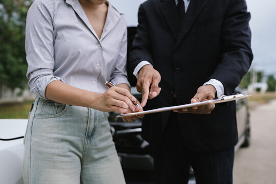 Man and woman standing by damaged car after accident, examining vehicle and filing insurance claim with agent for roadside assistance and repair.