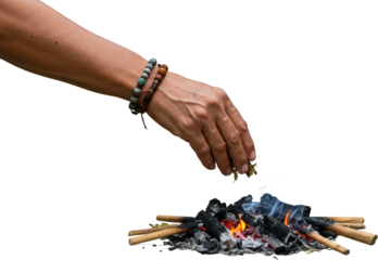 Person adding herbs to a small campfire hand close up with beaded bracelets