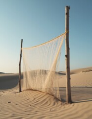 Old fishing net drying between wooden poles beside sandy dunes
