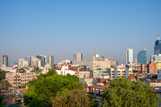 Elevated view of Mexico City skyline with modern and traditional buildings, trees, and clear sky, ideal for business, architecture, real estate and urban development stock.