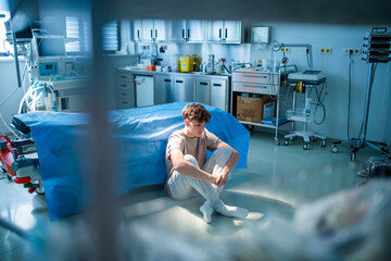 Teenage boy sitting depressed on hospital floor, struggling with mental health issues.