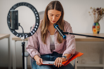 Young woman recording a podcast using a microphone and ring light