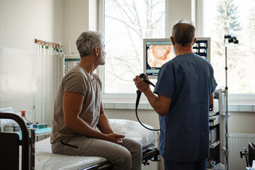 Doctor explaining colonoscopy results to patient using monitor images.