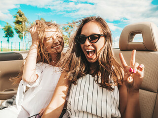 Portrait of two young beautiful and smiling hipster female in convertible car. Sexy carefree women...