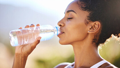 Woman drinking water with bottled water in her mouth against a bright natural background. Hydration and health care concept.