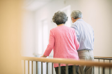 A hallway with handrails on both sides An older person walks with help from their caregiver holding their waist It feels focused and gentle