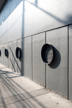 Perspective of circular vents on a grey concrete wall, geometric patterns and light contrast in modern architecture, ideal for design, urban backgrounds and stock visuals.