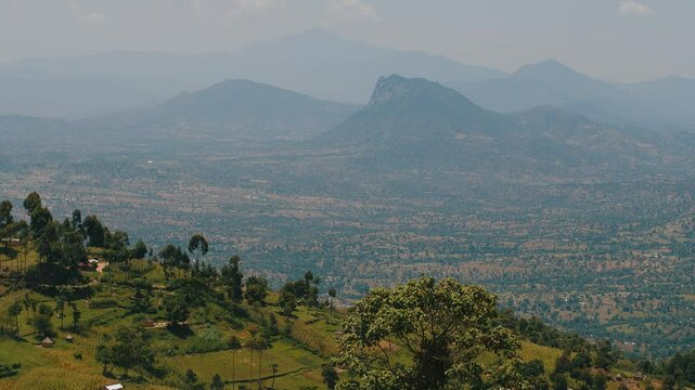 Panorama of hazy mountain peaks and the Great Rift valley with scattered on it buildings. Typical Kenyan bomas houses. Slow motion. View from above