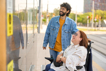 Caregiver assisting happy woman in wheelchair at tram stop - wheelchair and disability concept