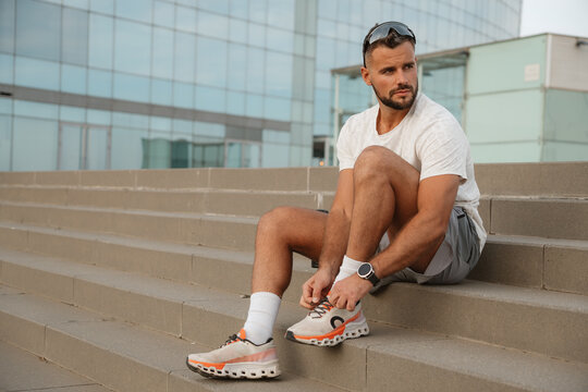 Male athlete tying running shoes while preparing for an urban workout, focused on fitness and motivation in a modern city setting