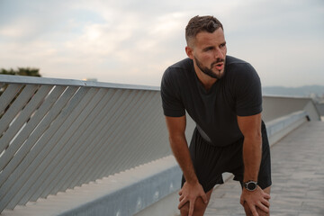 Exhausted male athlete resting on a bridge, catching his breath after an intense running workout, embodying determination and strength