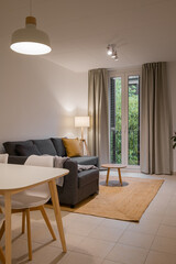 Close-up of a living room corner with gray sofa, yellow pillow, floor lamp and window with curtains