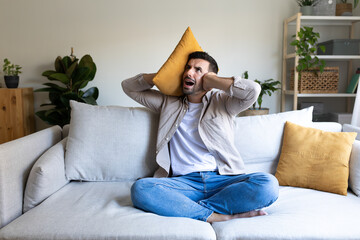 Distressed man covering ears because of upstairs loud noises.