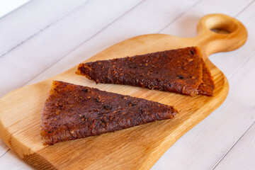 Close up of two folded dark brown triangular fruit pastille pieces resting on light wooden cutting board