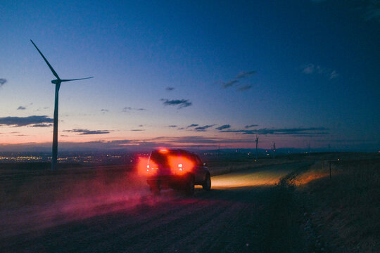 Red tail lights streak through the dust beneath wind turbines.