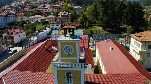 Establishing aerial footage of an old building with a clock tower in a small town in the mountain