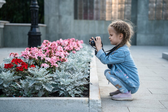 A young girl in denim takes a photo of flowers.