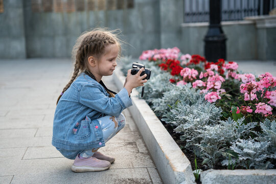 A young girl in denim takes a photo of flowers.