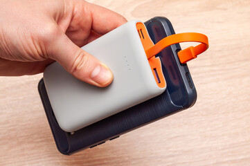 Close-up of a hand holding a power bank near a smartphone with orange accents on a wooden surface.