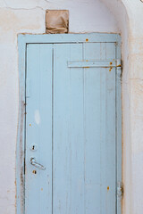 Rustic light blue wooden door in Plaka village, Milos island, framed by whitewashed walls and aged textures typical of Cycladic architecture