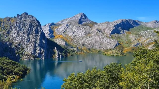 Idyllic peaks with lake in Riano, Spain. Motorboat navigating tranquil lake amidst majestic peaks.