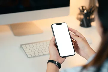 Fotobehang Close up of woman holding smartphone with blank screen at modern desk © Prathankarnpap
