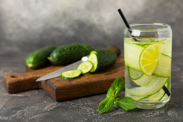Cucumber water with lemon, lime and mint on a wooden table. Water infused with sliced ​​cucumber in a drinking glass. Tonic refreshing drink. Cucumber lemonade.Summer natural cooling drink.Copy space