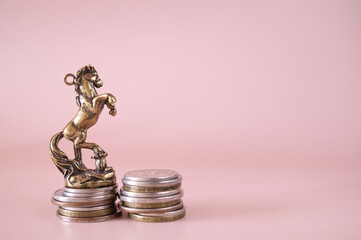 A statuette of a horse with coins on a pink background.