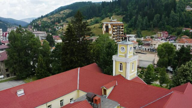 Establishing aerial footage of an old building with a clock tower in a small town in the mountain