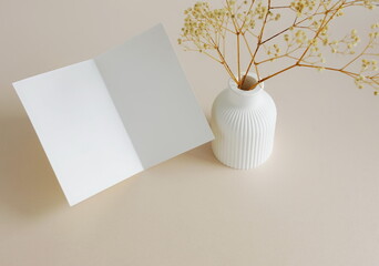 Greeting Card mockup, folded empty white blank,  dry flowers in a vase, on beige background. copy space. Minimalist aesthetic composition