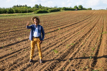 African farmer is standing in his freshly sown agricultural field. He is cultivating clover.