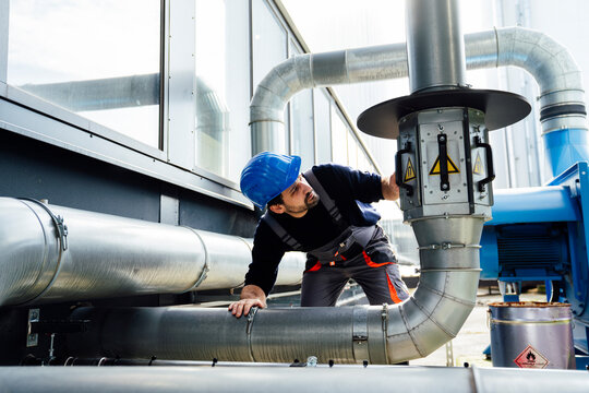 Engineer inspecting industrial pipes outdoors wearing a blue hard hat