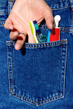 Closeup of a hand holding a toothbrush and toothpaste in a denim jeans pocket