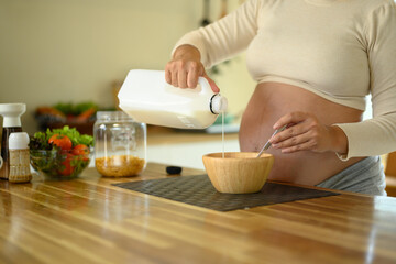 Hands of a pregnant woman making a morning meal in a bright kitchen