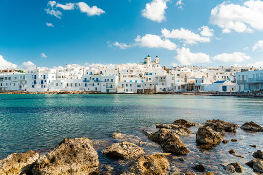 Scenic view of the traditional white houses in Naousa, Paros with a rocky shoreline and blue sky.