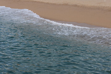 Waves gently wash onto a sandy beach, blending turquoise sea with golden shoreline under soft light.