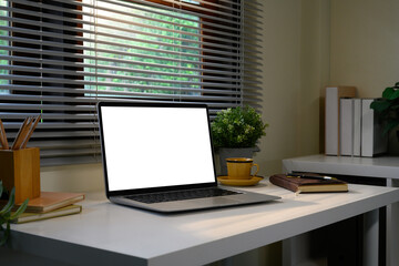 Modern home office desk with a blank laptop screen, notebook, and plants by the window