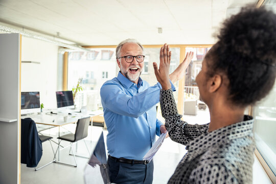 Cheerful businessman doing high-five with female colleague in office