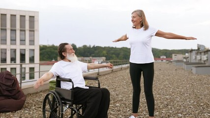 Senior man in wheelchair and woman performing fitness stretches together on outdoor rooftop. Smiling expressions suggest positivity, unity. Concept showcases active lifestyle, aging gracefully