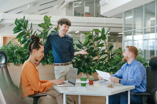 Businesspeople having a discussion in a modern office setting with plants and laptops