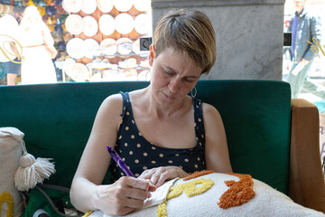Woman sitting comfortably in a cafe, diligently writing in a notepad, with a backdrop of ceramic plates displayed in a shop window