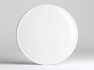 Simple white plate is sitting on a plain surface and catching the light, it makes a subtle shadow that adds a bit of depth to the clean scene.