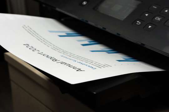 Closeup of printed business document emerging from office printer, concept of financial reporting and document output
