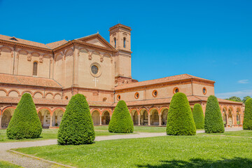 Saint Christopher church of Charterhouse of Ferrara, with its cloister and facade on a sunny day, is surrounded by manicured lawns and cone-shaped bushes in Ferrara city of Italy