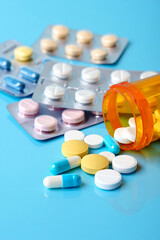 Close-up, high-resolution image of various pharmaceutical tablets and capsules of different shapes, sizes and colours neatly arranged on a clean white or light blue background.