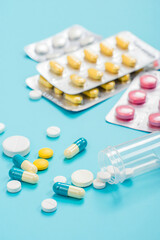 Close-up, high-resolution image of various pharmaceutical tablets and capsules of different shapes, sizes and colours neatly arranged on a clean white or light blue background.