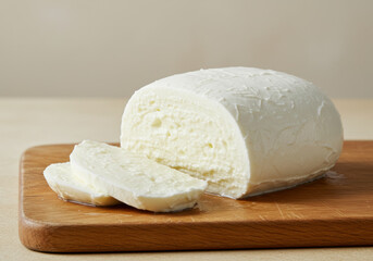 A close up shot of a loaf of mozzarella cheese, partially sliced on a wooden board.