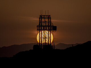山に沈む夕陽がシルエットの鉄塔と重なる瞬間