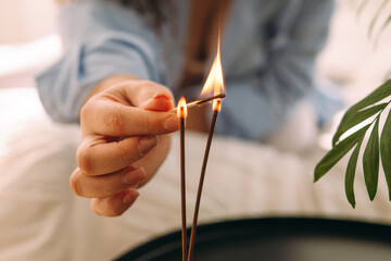 Close-up of a woman's hands lighting incense sticks in a bedroom.